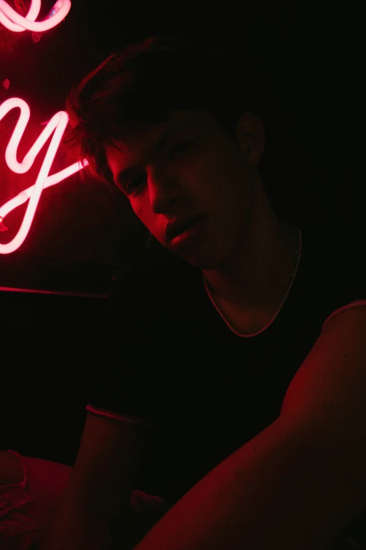 a young person is sitting by a neon sign