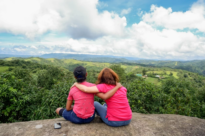 two people are sitting on a stone overlooking an ocean