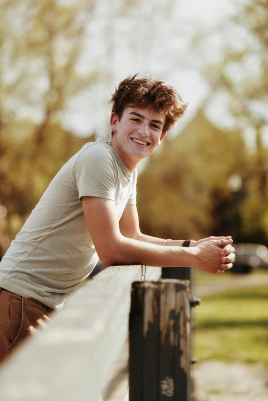 a smiling young man leans on a fence rail