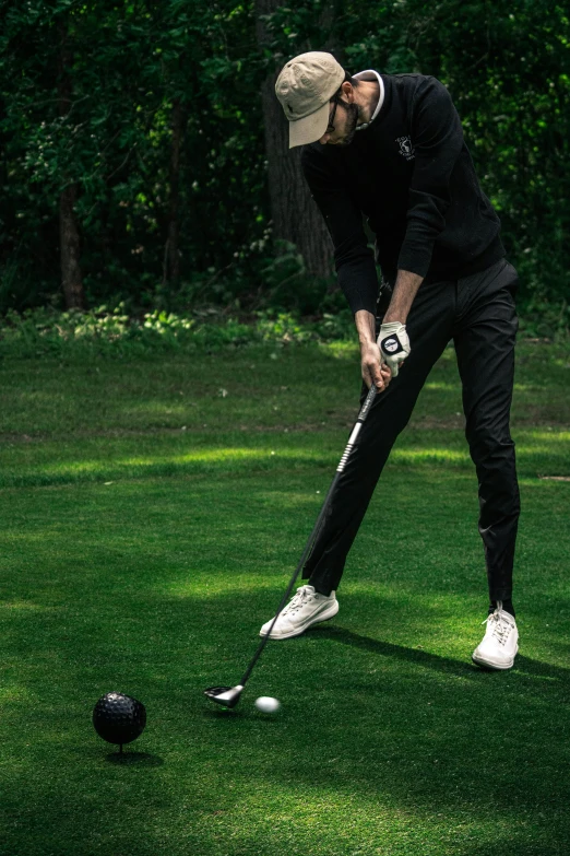 a man wearing all black, putting a putt into a ball