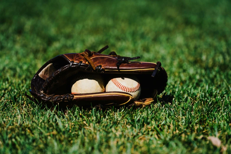 a baseball glove and two baseballs sitting on a green field