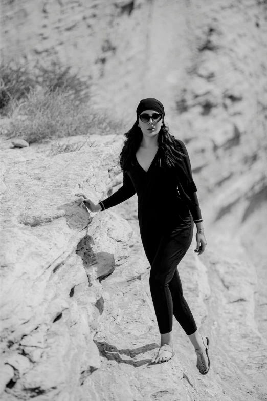 a woman in black and white with sunglasses on walking on a mountain