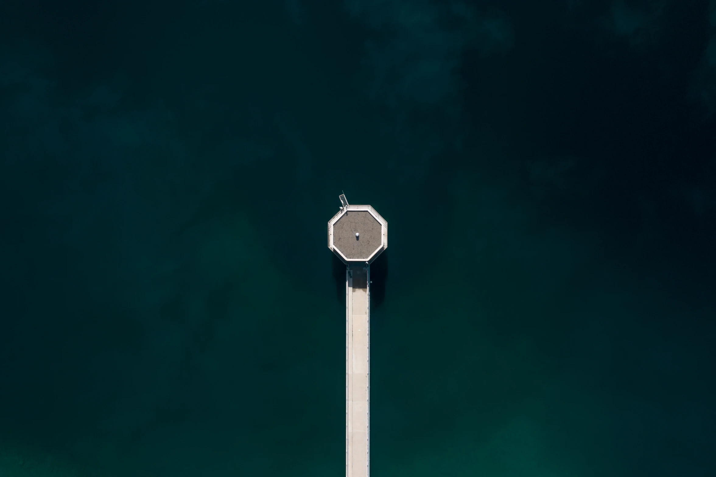 a clock sits atop an ocean buoy with a pier underneath it