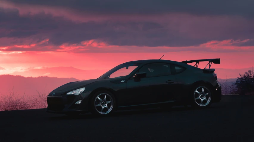a compact, black car parked on the road as the sun sets