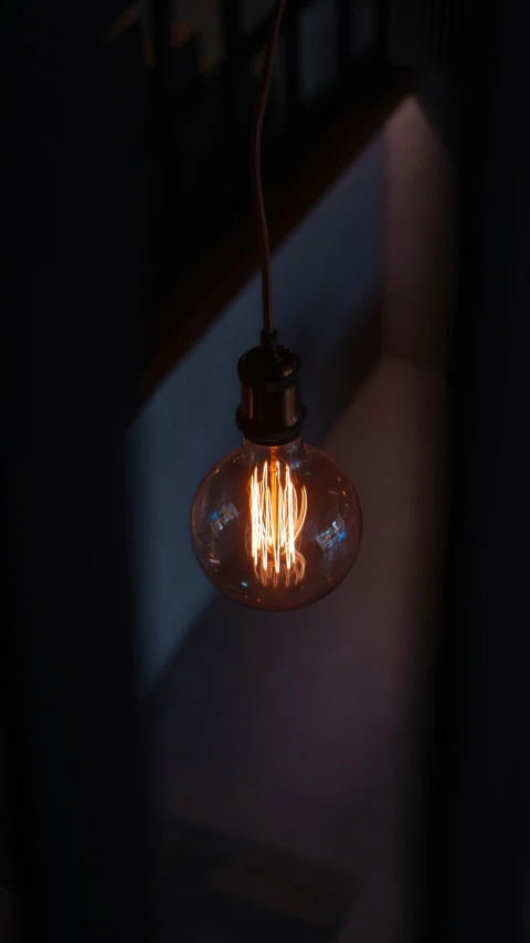 an old style light bulb hangs from a dark fixture