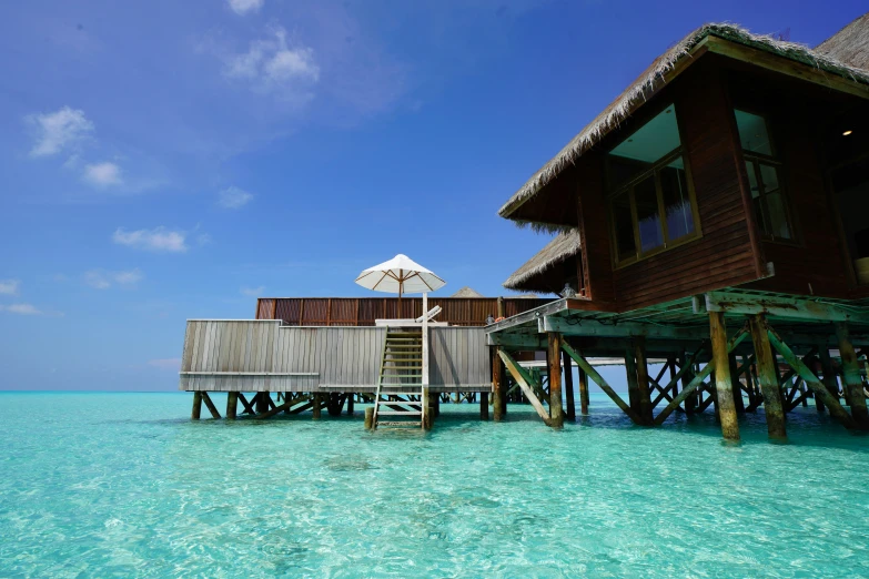 a house on stilts in the ocean next to a dock with an umbrella