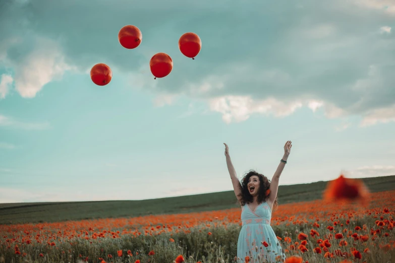 a woman is standing in a field with her arms up while flying red balloons