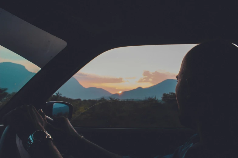 a man sitting in a car driving along side the mountains