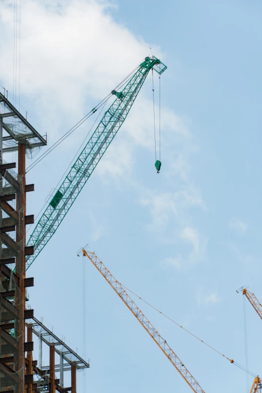 three cranes against a blue sky with clouds