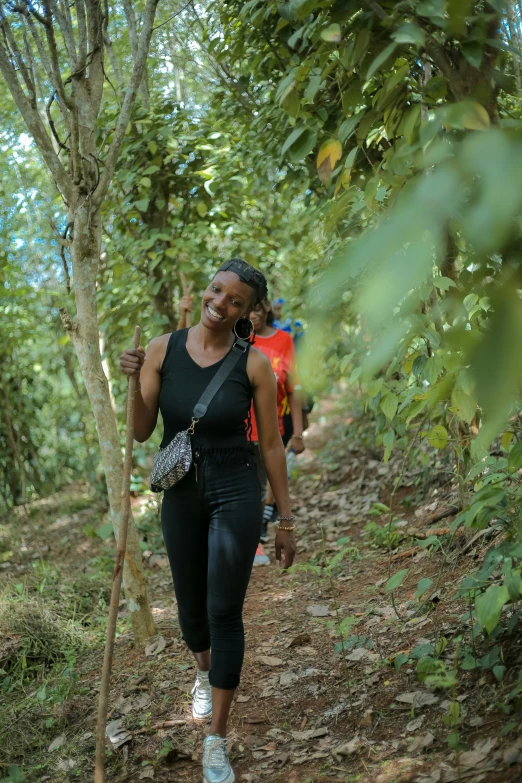 a woman in black pants and a bag walks through the trees