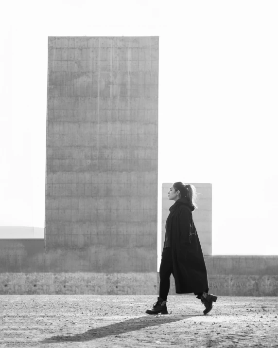 a woman in a black coat walks near a tall building