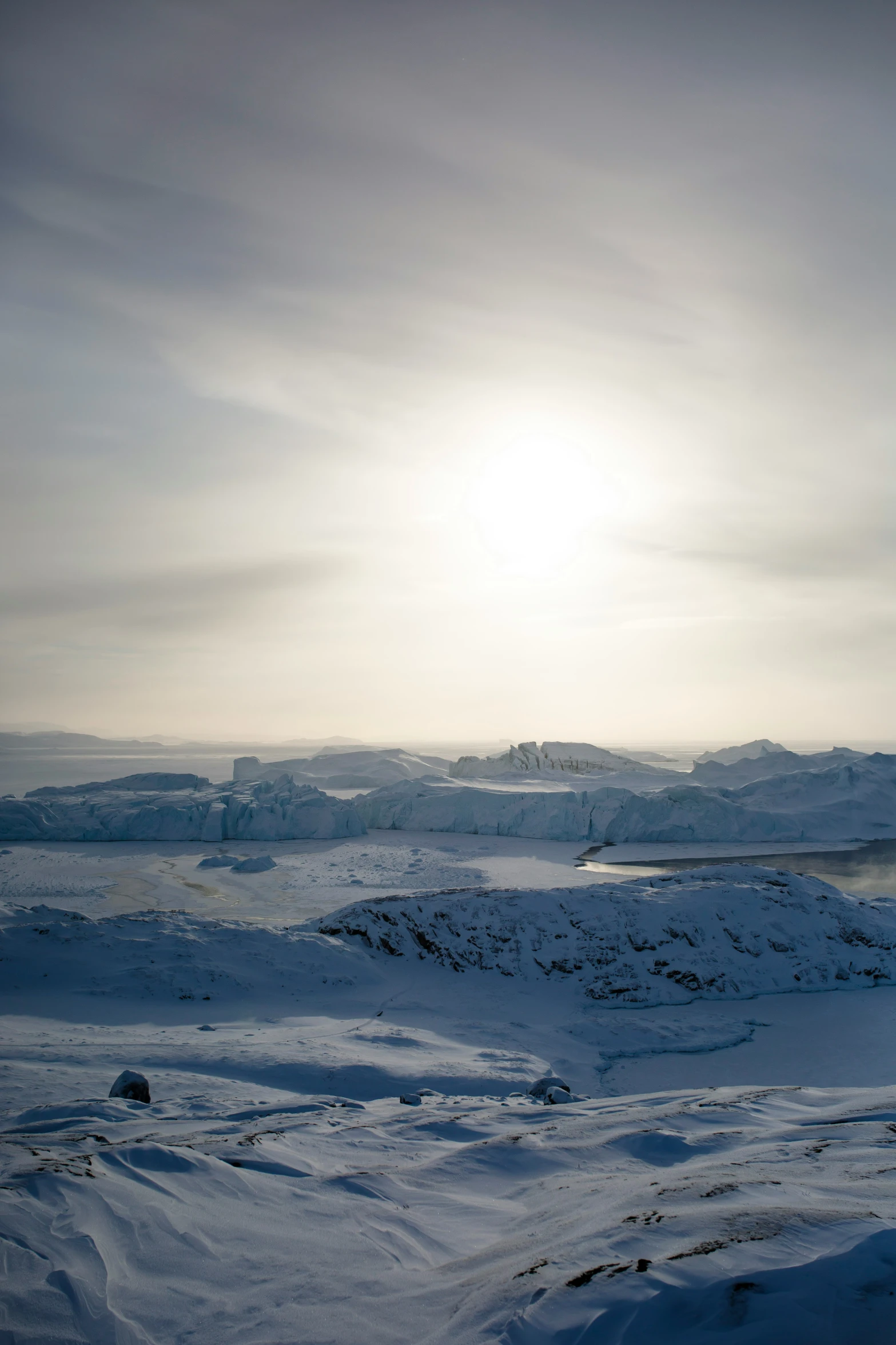 sun peeking through cloudy skies over snowy hills