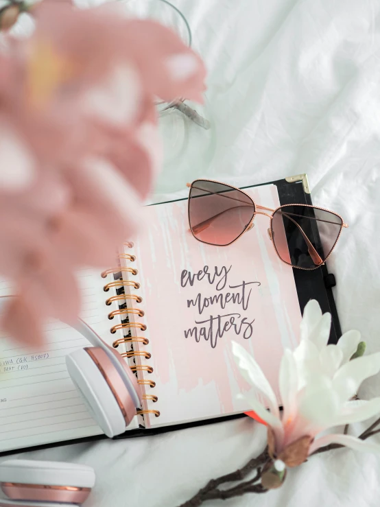 a note book and sunglasses on top of a bed