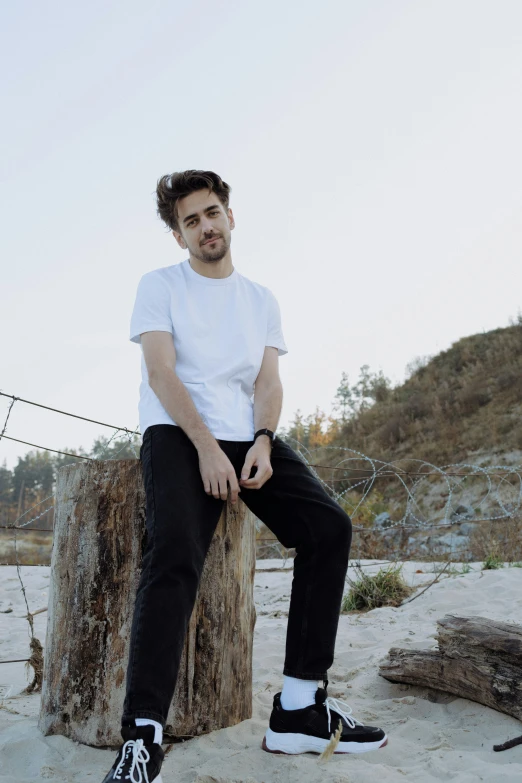 a young man is sitting on a stump with his leg on a tree