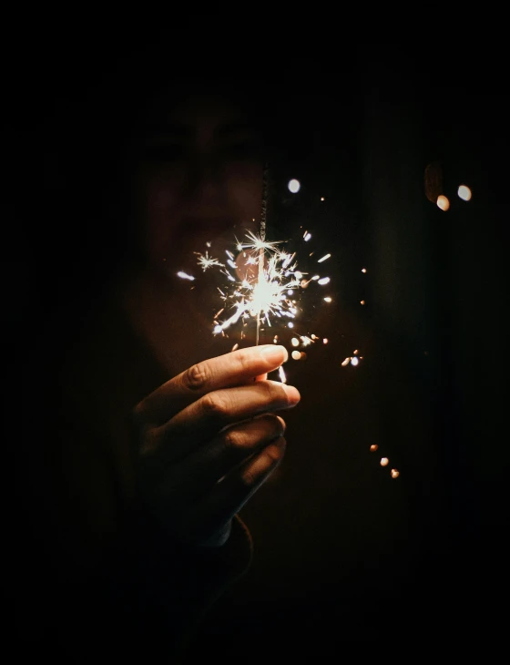 a person holding a lite up firecrot in the dark