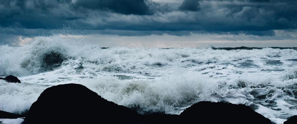 a body of water surrounded by black rocks under a dark cloudy sky