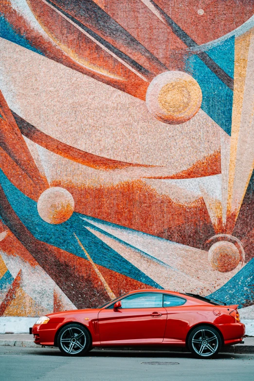 a red sports car is parked in front of a mural