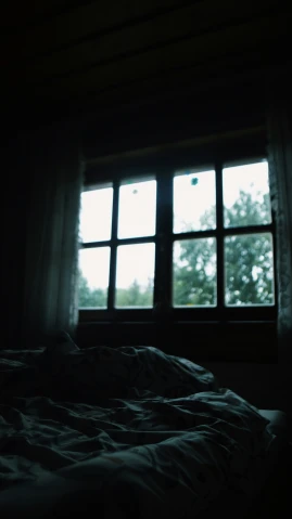 a dark room with a bed, window and curtains