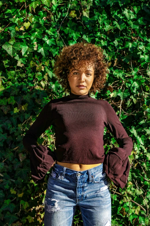 woman standing in front of green vegetation, with arms on hips