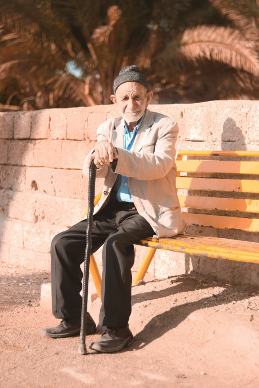 an elderly man sitting on a bench while holding a cane