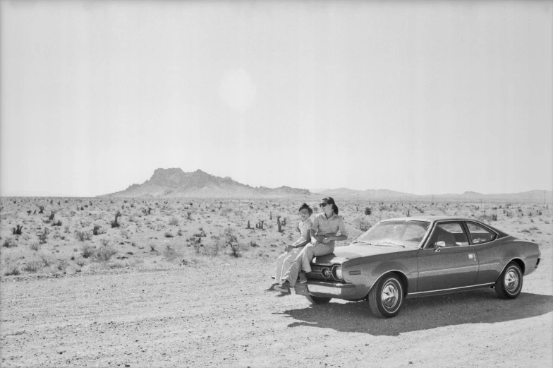 two women sitting on the hood of a parked car