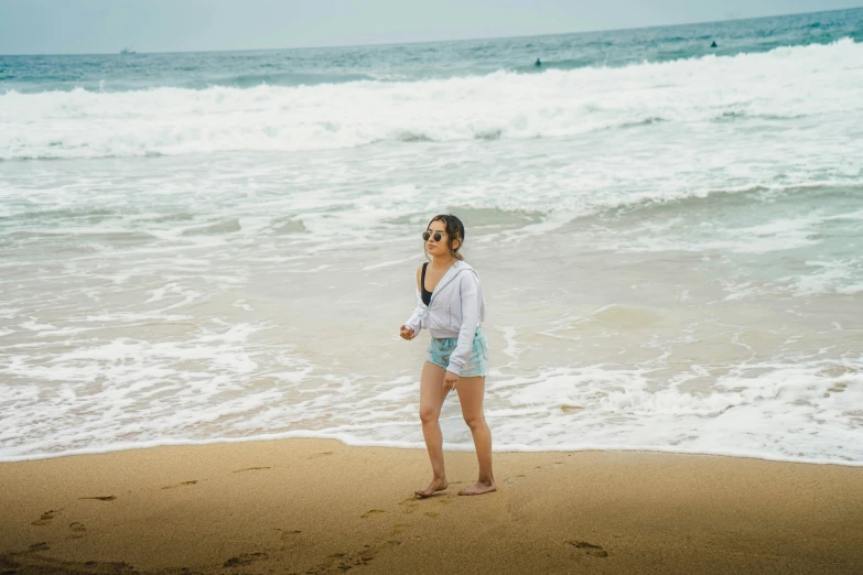 there is a young woman standing on the beach, and talking on her cell phone