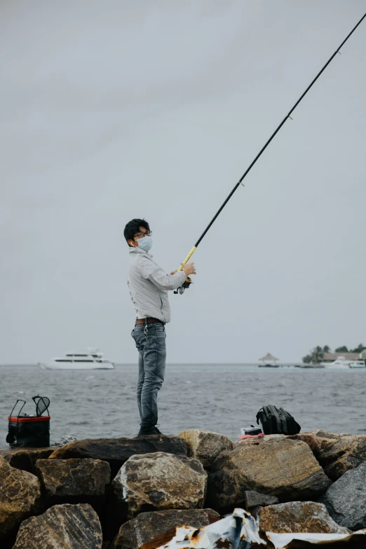 a man holding onto a fishing rod on a rock with the water in the background