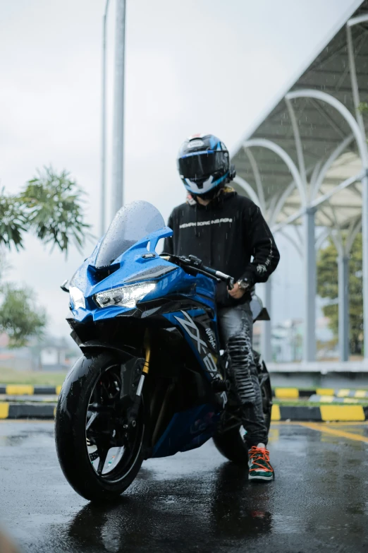 a man riding a blue motorcycle on top of a wet road