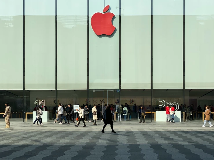 people walking and sitting on the steps in front of a building with the logo of apple on it