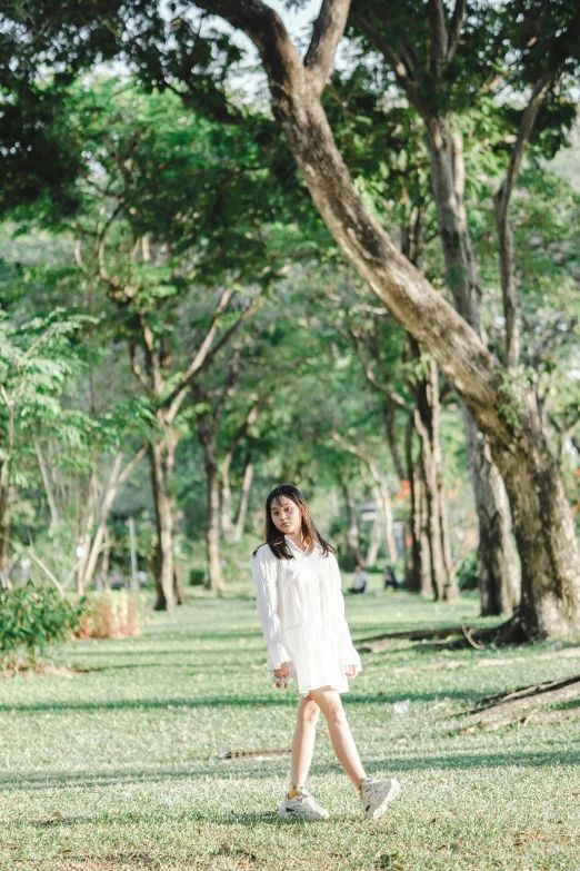 girl in white dress walking through grassy area by tree