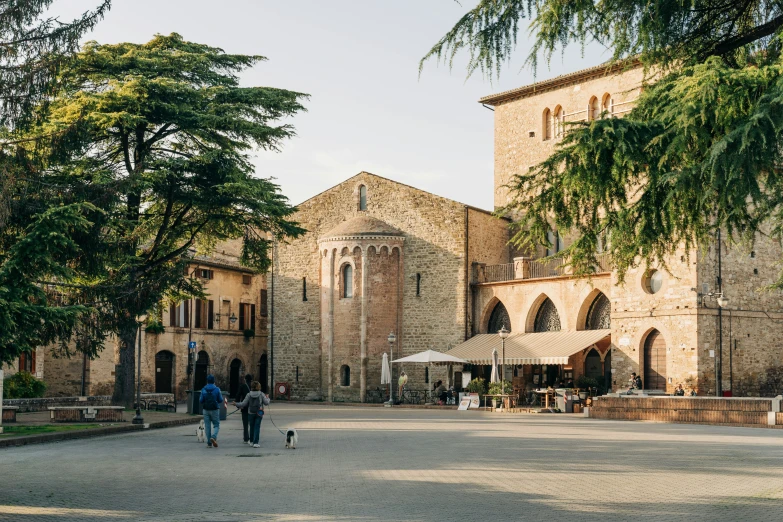 people walk through the middle of a plaza with an old brick building in the background