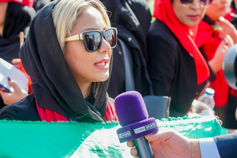 woman in black coat with microphone talking to reporters