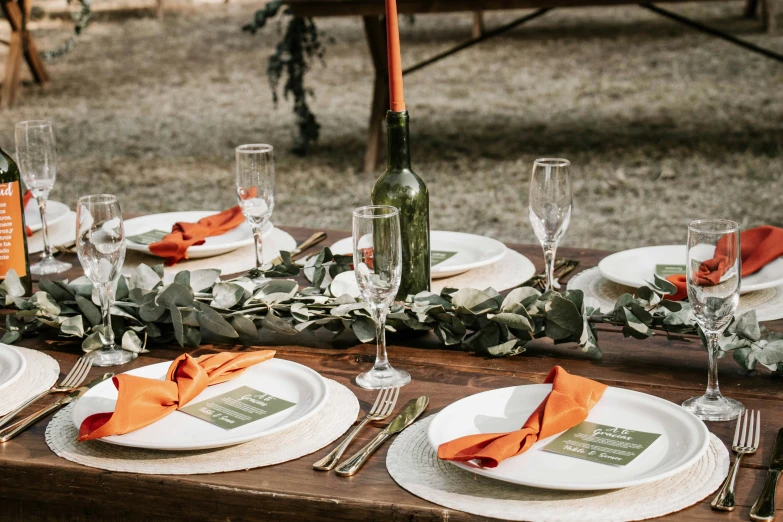 a table setting with white and orange dinnerware, flowers, wine bottles, and napkins