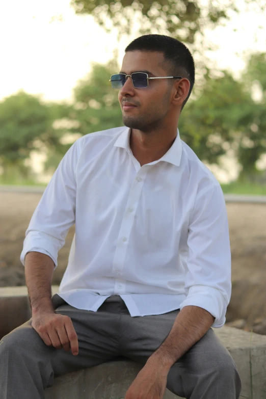 a man wearing sunglasses sitting in front of trees