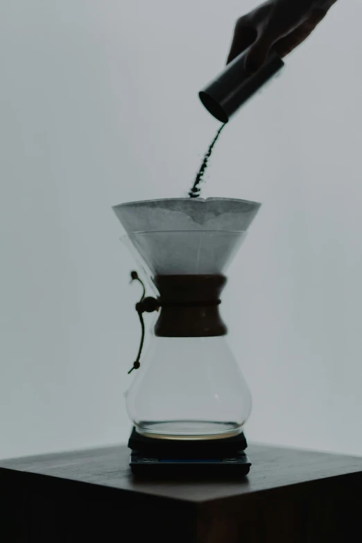 someone pours water from a pourer into a glass pitcher