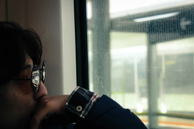 a man sitting by a window, wearing glasses