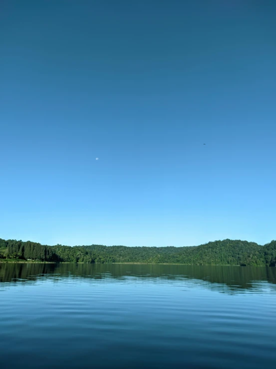 a calm lake is lined with trees under a blue sky