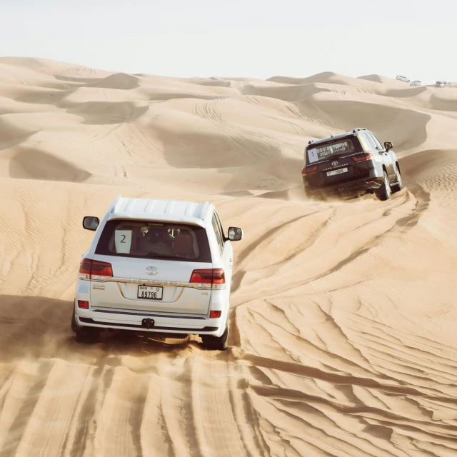 two trucks driving through the desert in the sand