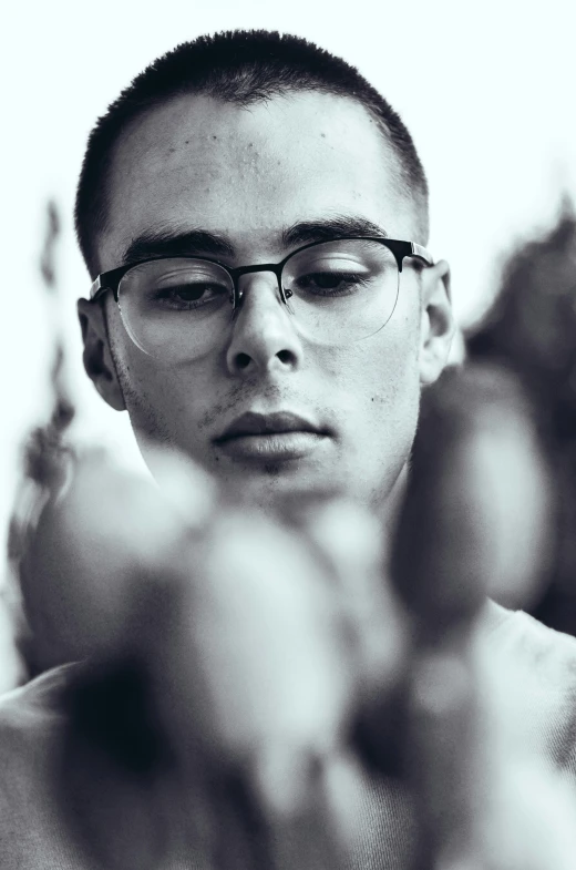 a shirtless young man wearing glasses while standing next to plants