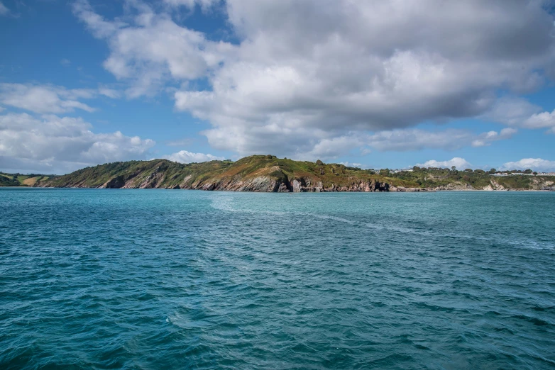 a blue ocean with rocks and some clouds in the background