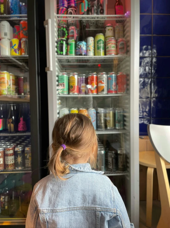 a little girl sitting in front of a refrigerator that has sodas and juice