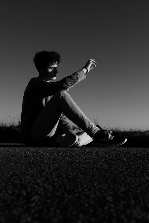 black and white image of man sitting in the grass on the edge of a road