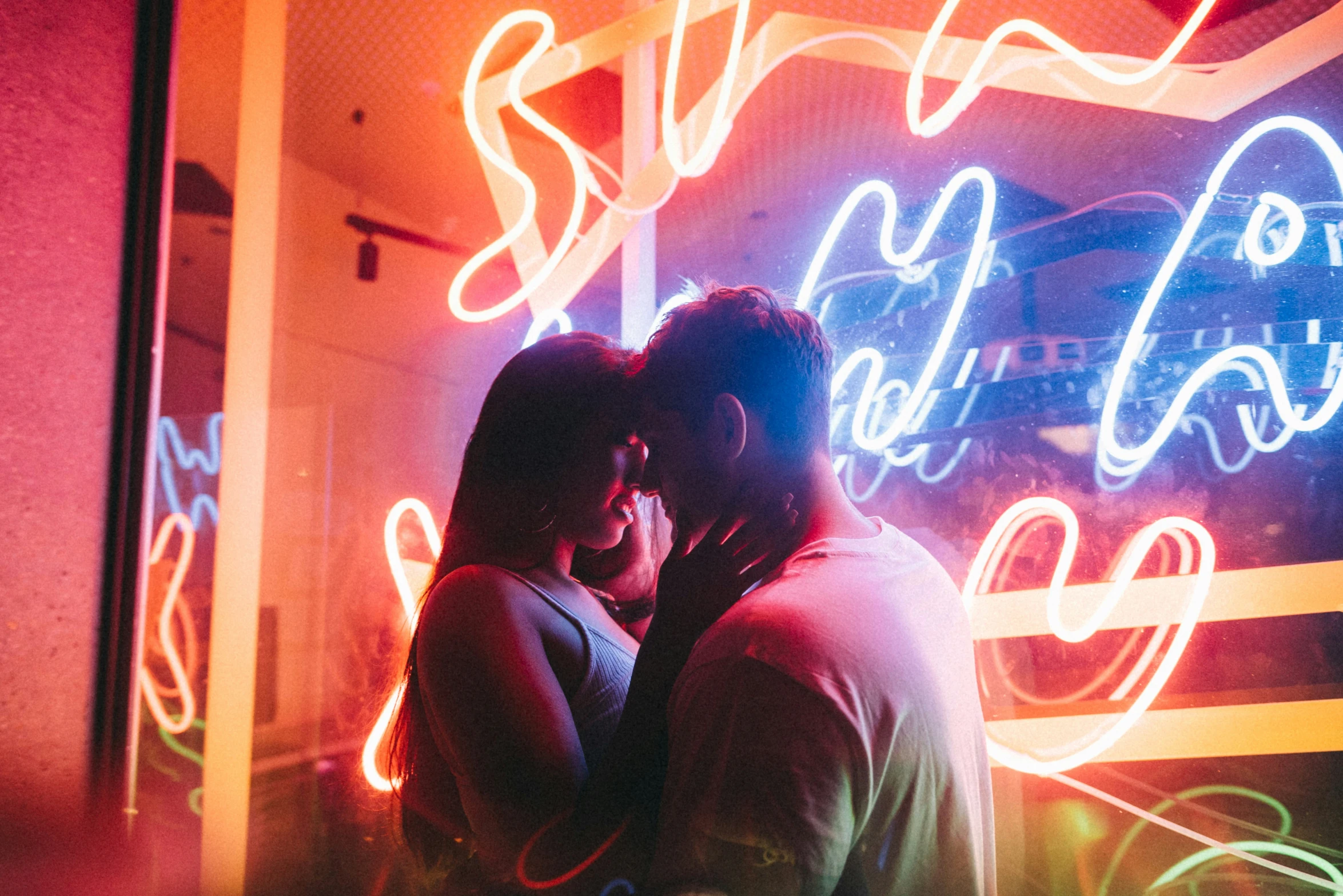 two people are hugging and a neon light background is seen