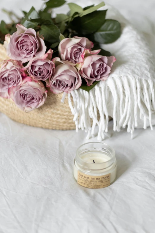 a rose candle sits next to pink roses and a blanket