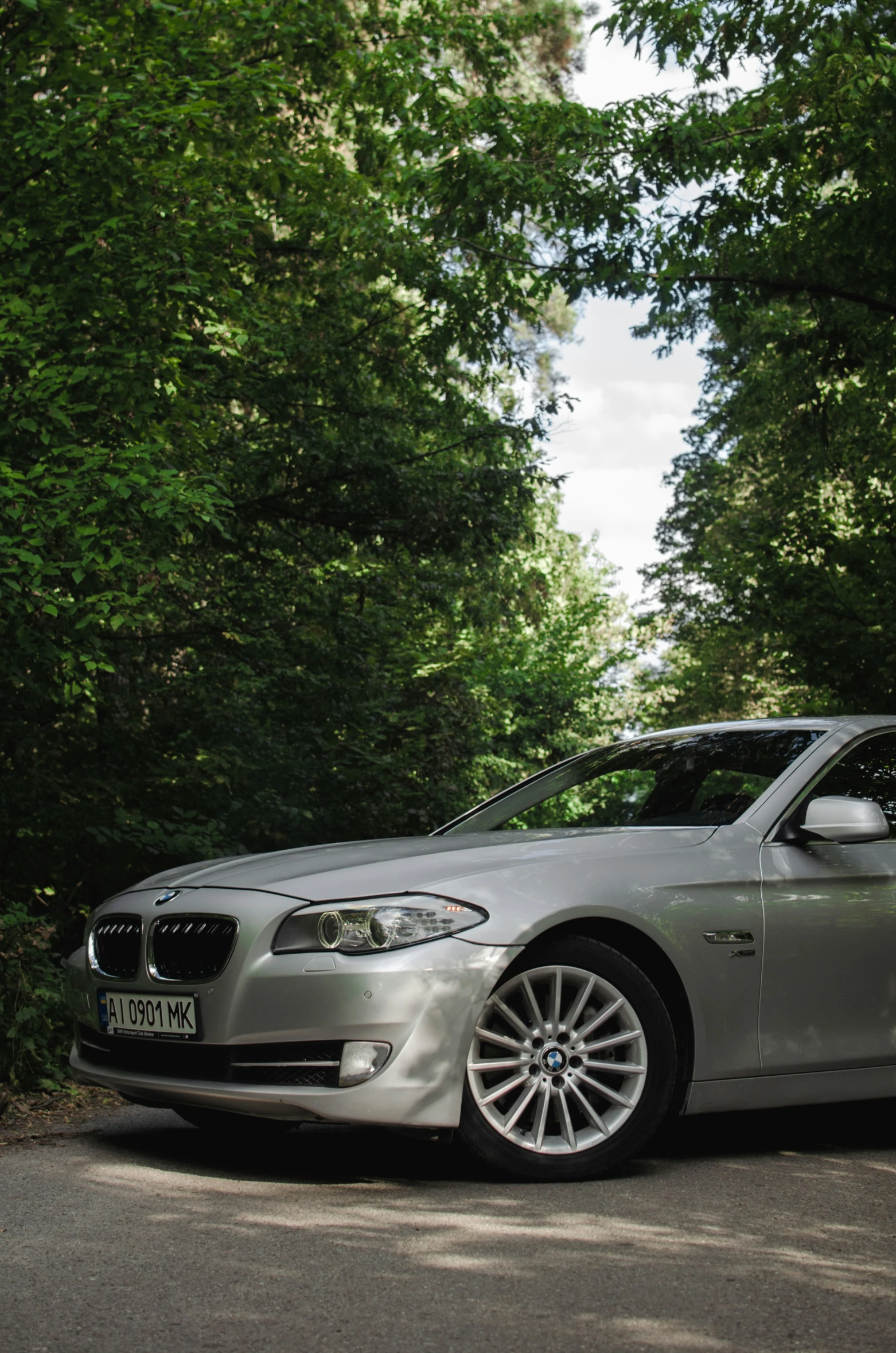 a silver bmw car is parked along side a wooded area