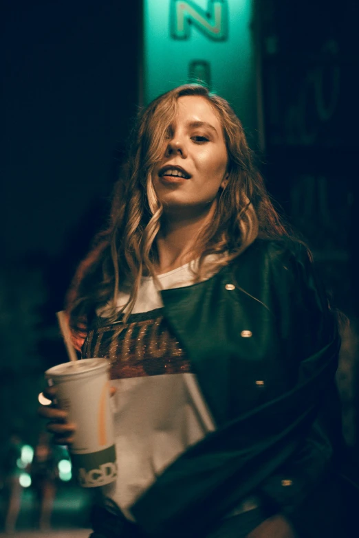 woman drinking  chocolate from cup on sidewalk near neon sign