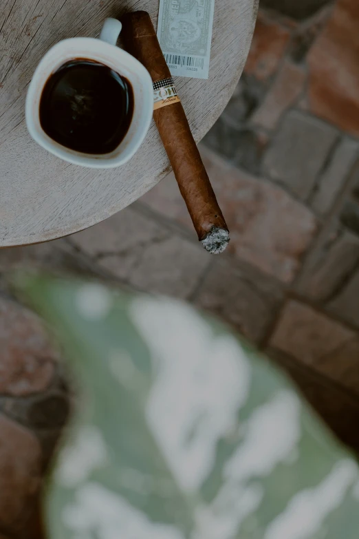 a single cigar sits on a table with an empty cup of coffee next to it