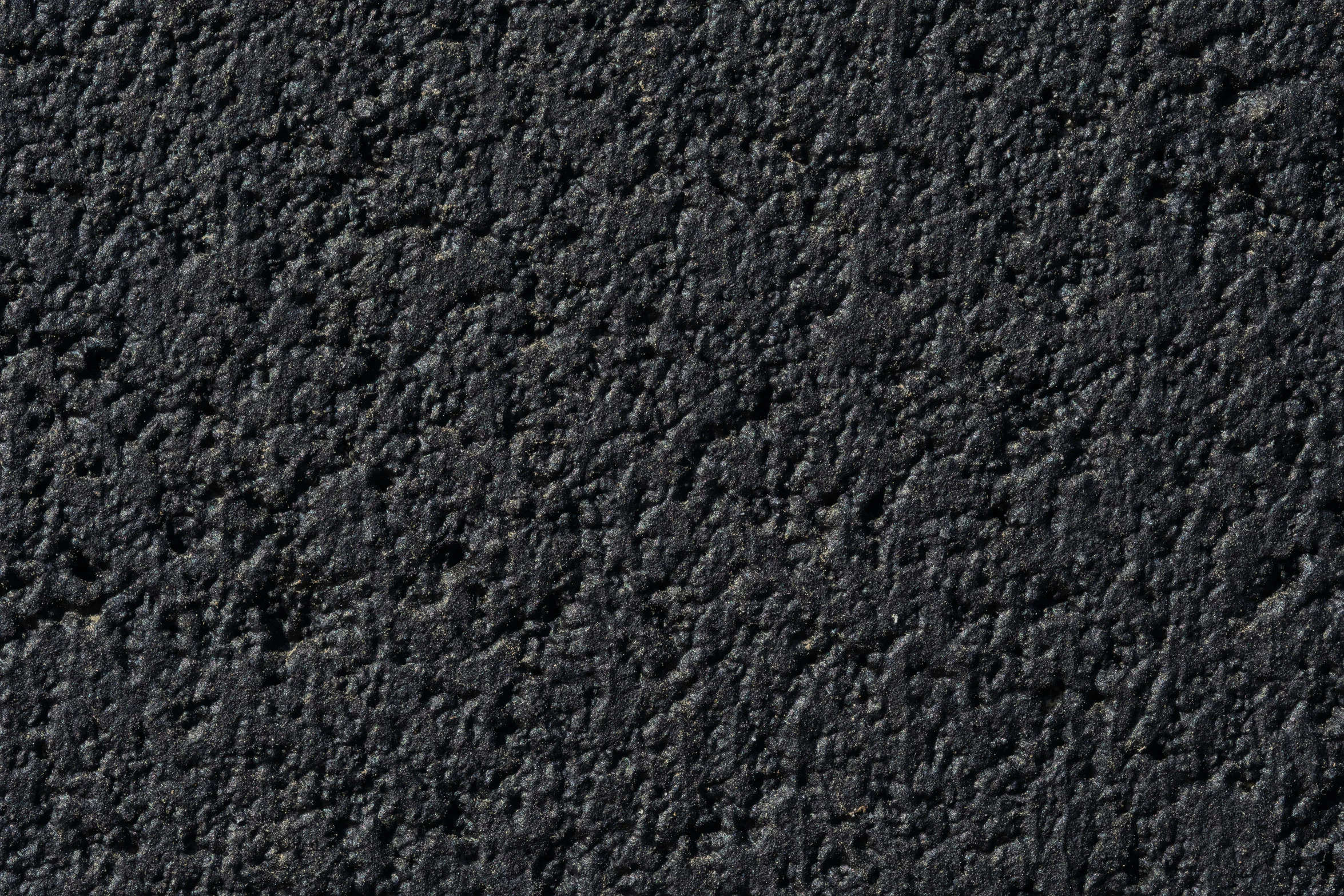 some grey asphalt with black dots near some rocks