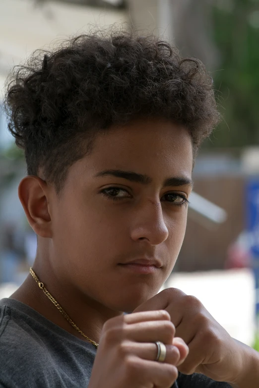 the young man is wearing an open necklace and is looking away from the camera