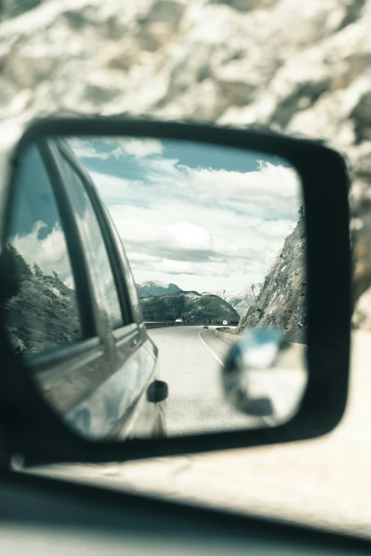 the side view mirror of the car shows mountains